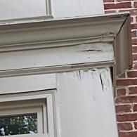 Close-up of a door frame with peeling, cracked, and weathered white paint on the molding and trim.