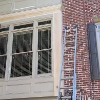 A silver aluminum extension ladder leaning against a brick wall next to a large, multi-paned window.