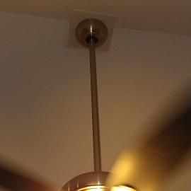 A metal ceiling fan mount and downrod extending from a white ceiling, partially obscured by blurred, spinning fan blades.