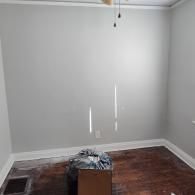 An empty room with gray walls, white trim, dark wood flooring, and a small box in the center.