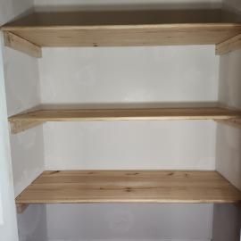 Three unfinished wooden shelves installed in a closet with white walls.
