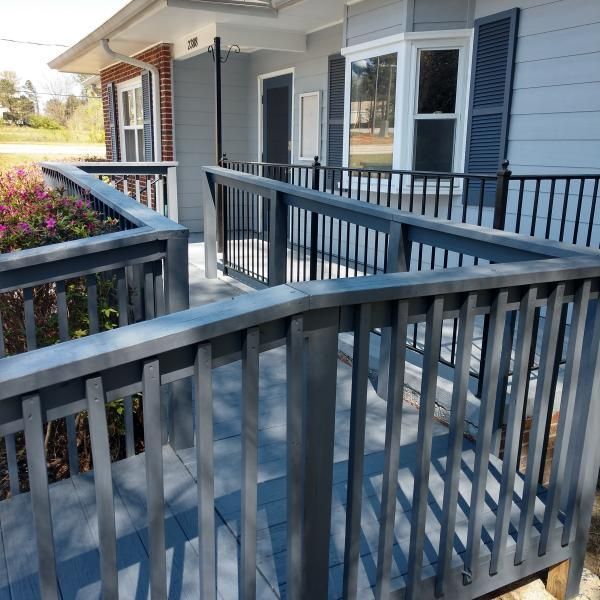 A gray wooden wheelchair ramp with railings leads to the entrance of a house with gray siding.
