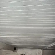 A ceiling with light-colored horizontal wood paneling and a beam near the bottom, viewed from below.