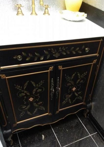 A black bathroom vanity with gold floral detailing, brass hardware, and a white marble countertop.