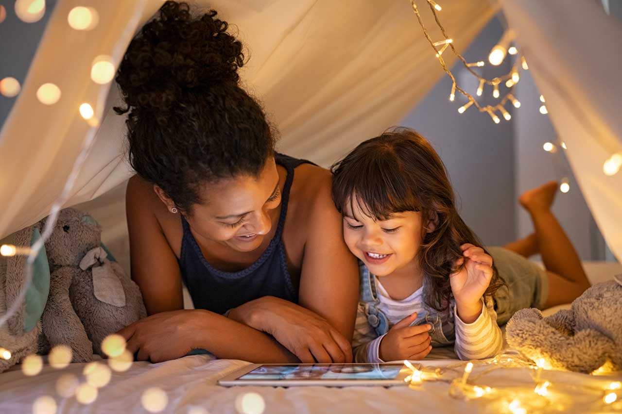 Mother-and-daughter-using-digital-tablet-inside-illuminated-cozy-hut