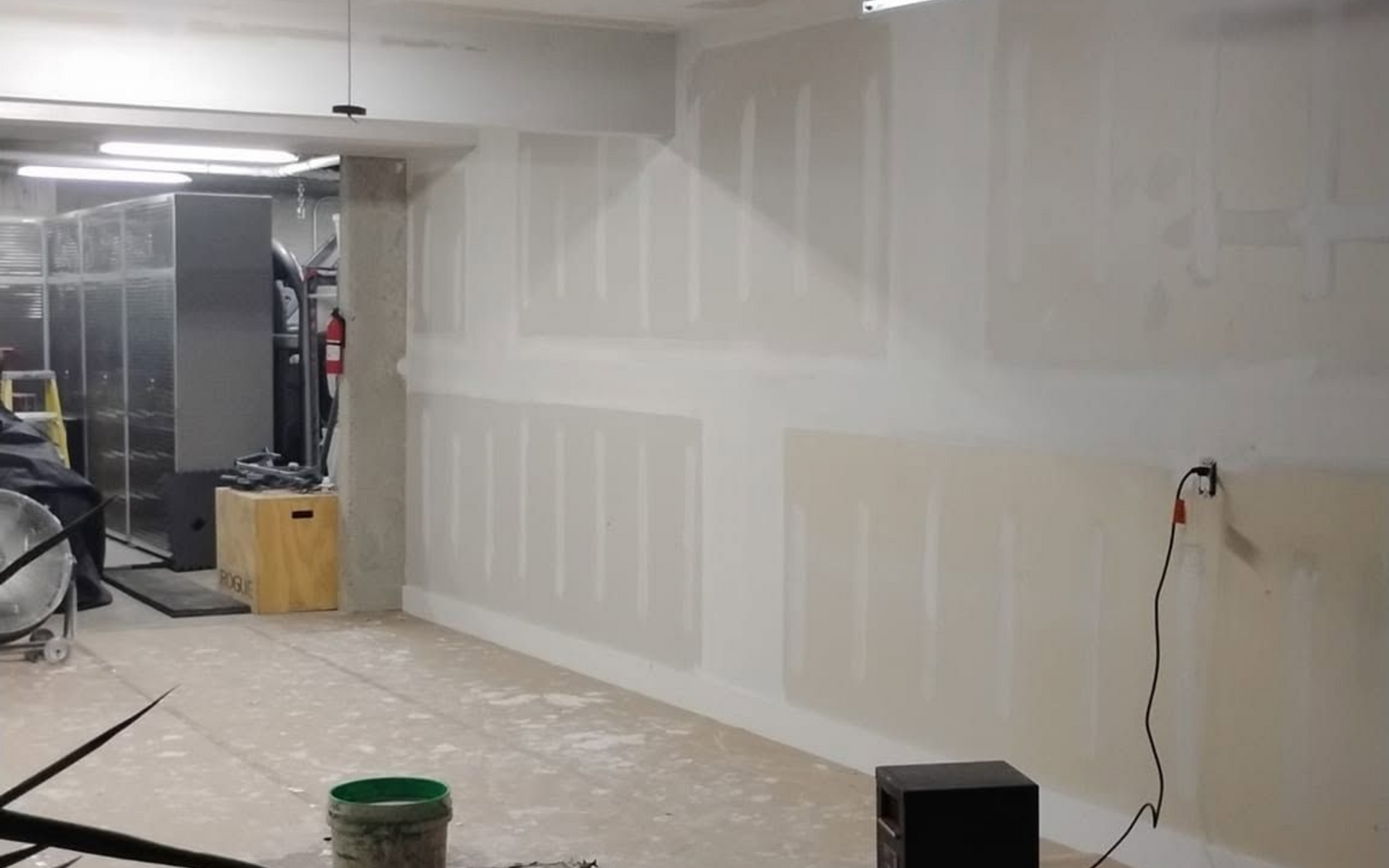 Empty room under renovation with drywall, exposed floor, and construction tools.