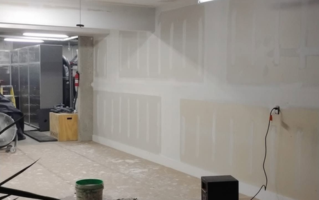 Worker in orange shirt smoothing drywall with a trowel in a partially finished room