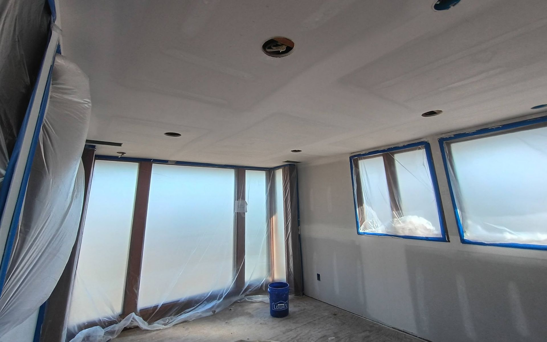 Partially finished room with plastic-covered windows and a blue bucket on the floor