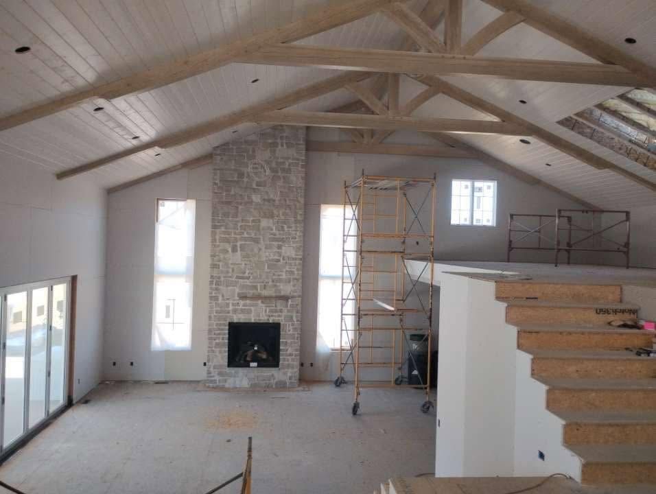 Interior of a new house under construction with exposed ceiling beams, stone fireplace, and scaffolding.