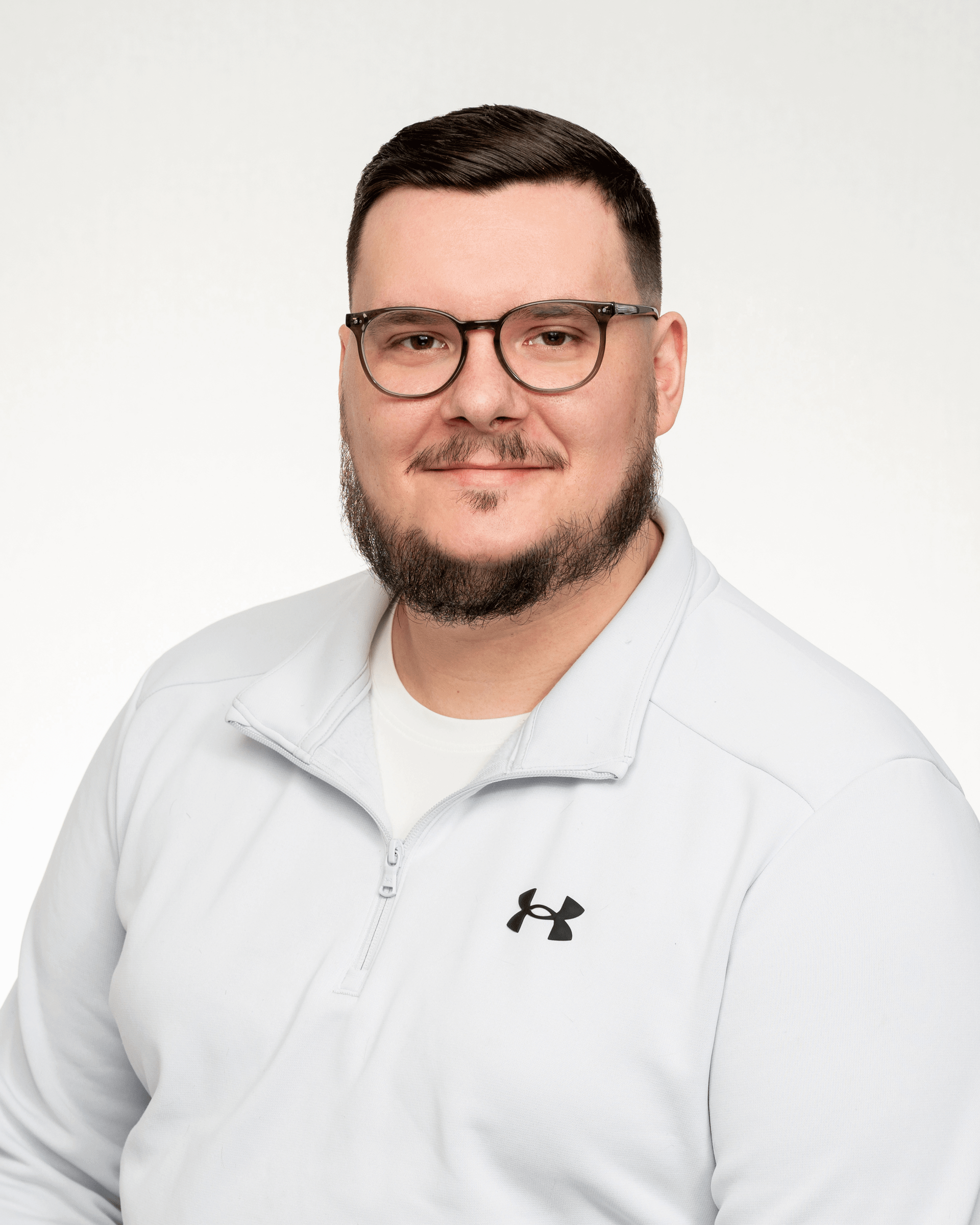 a man with a beard and glasses is wearing a white under armour jacket .