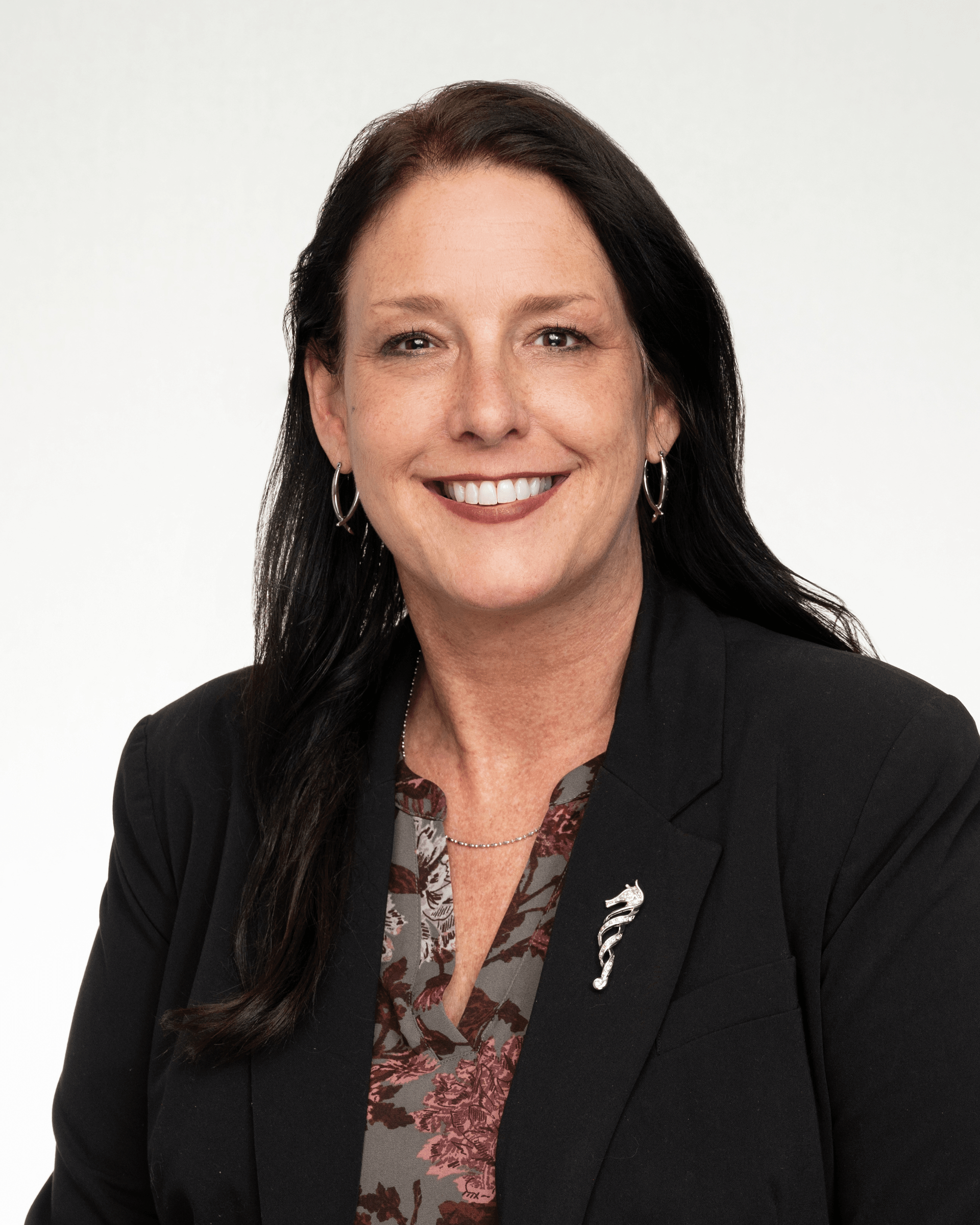 a woman in a black jacket and floral shirt is smiling for the camera .