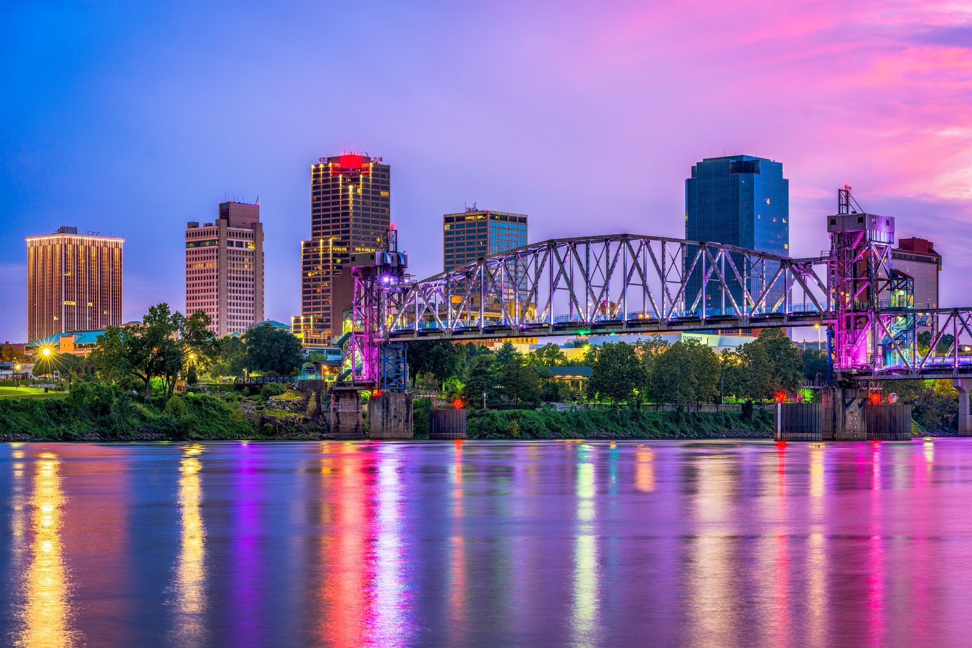 a bridge over a river with a city skyline in the background at night .