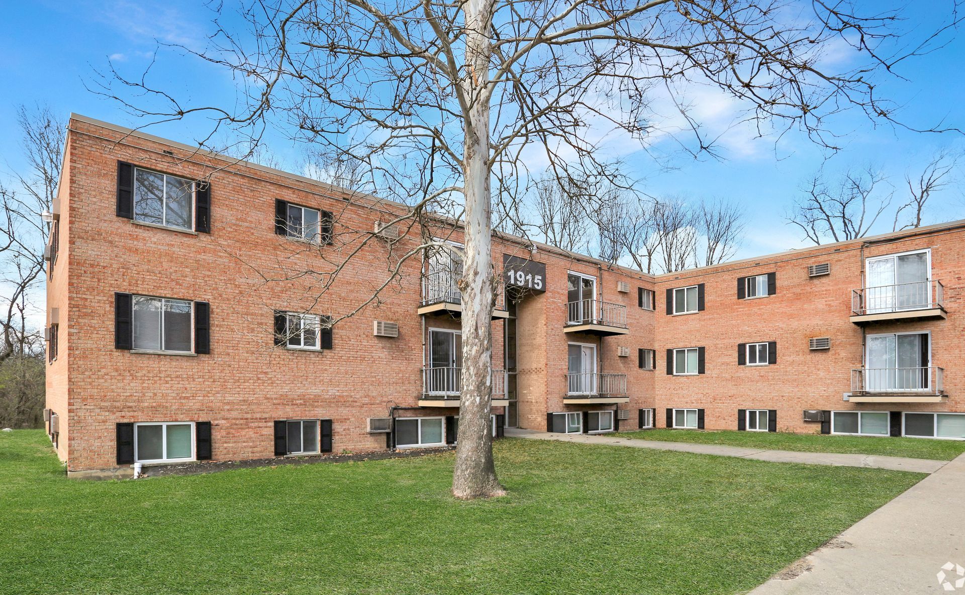 Brick apartment building at Overlook at Wyoming with balconies, black shutters, a green lawn, and mature trees.