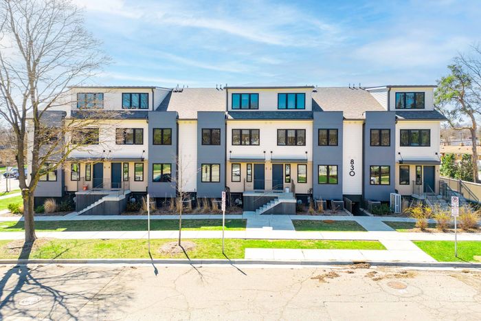 Row of modern beige townhouses with black-framed windows and small front steps along a tree-lined street
