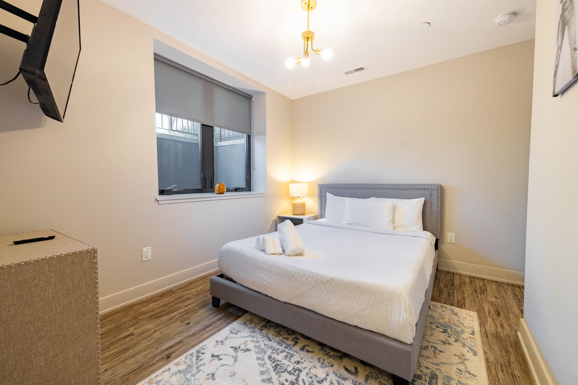 Modern bedroom with gray bed, white bedding, bedside lamp, and window with blinds