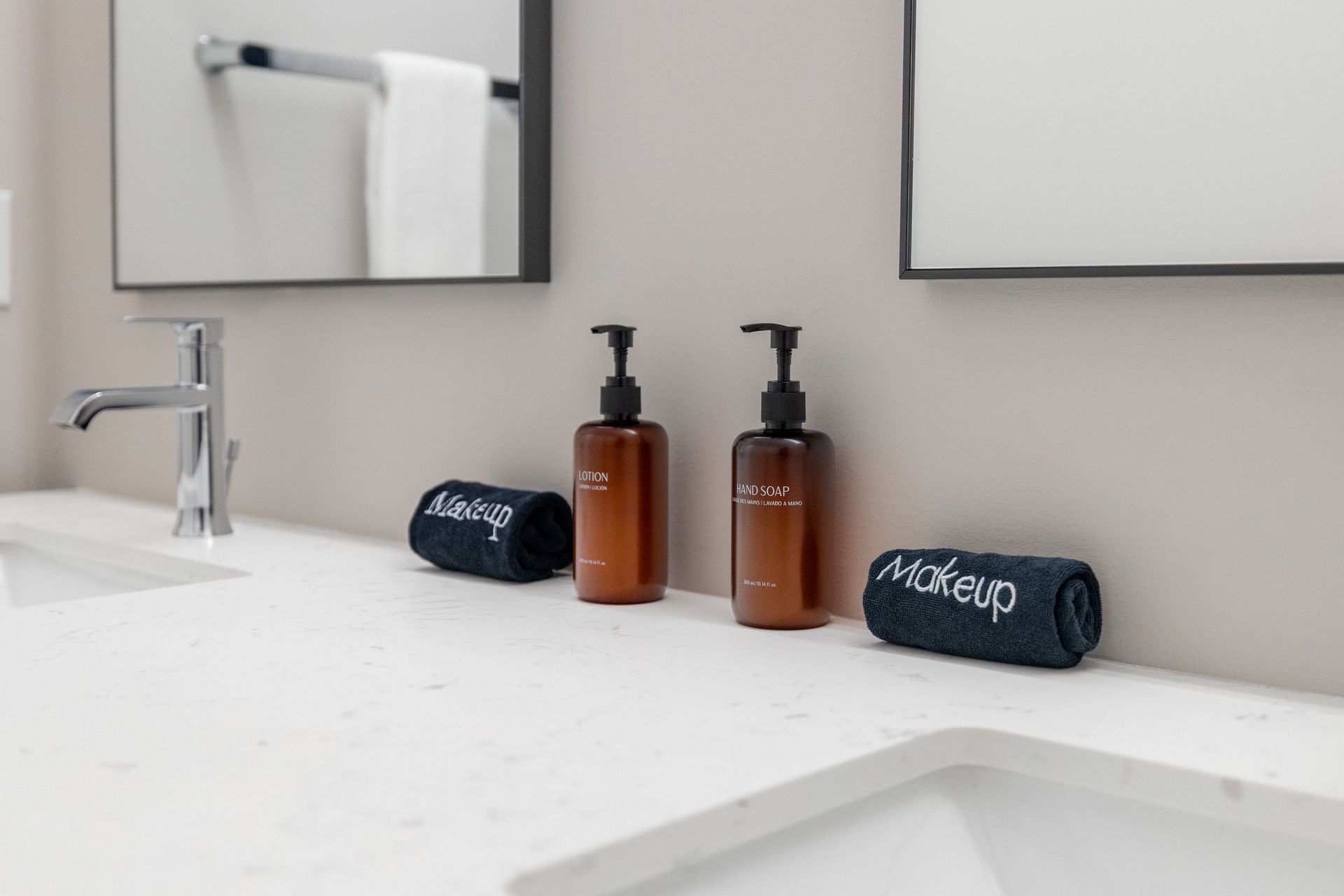 Modern bathroom vanity with white countertop, two amber soap dispensers, and folded dark towels near a sink.
