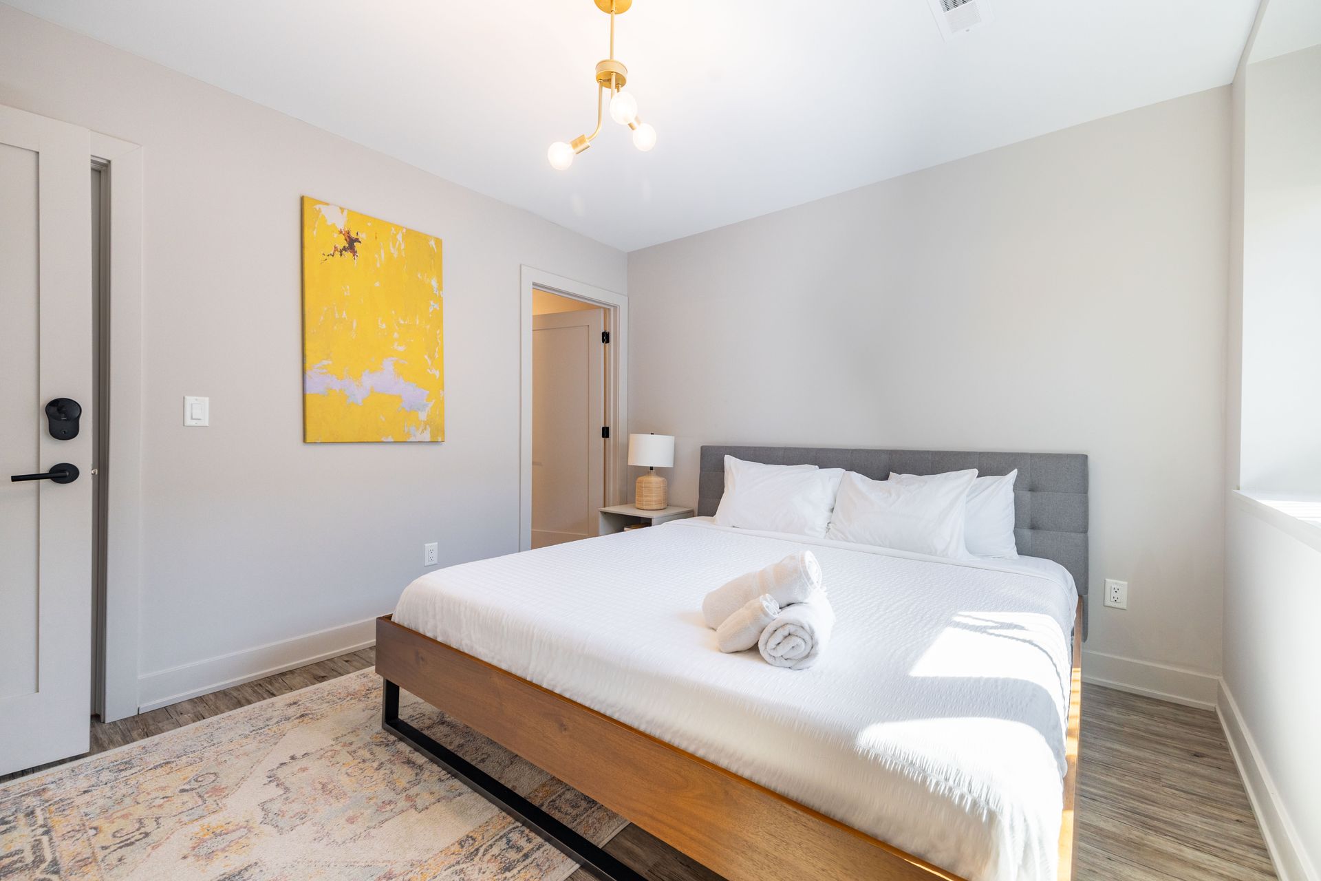 Bright bedroom with a bed, white bedding, yellow wall art, and a patterned rug