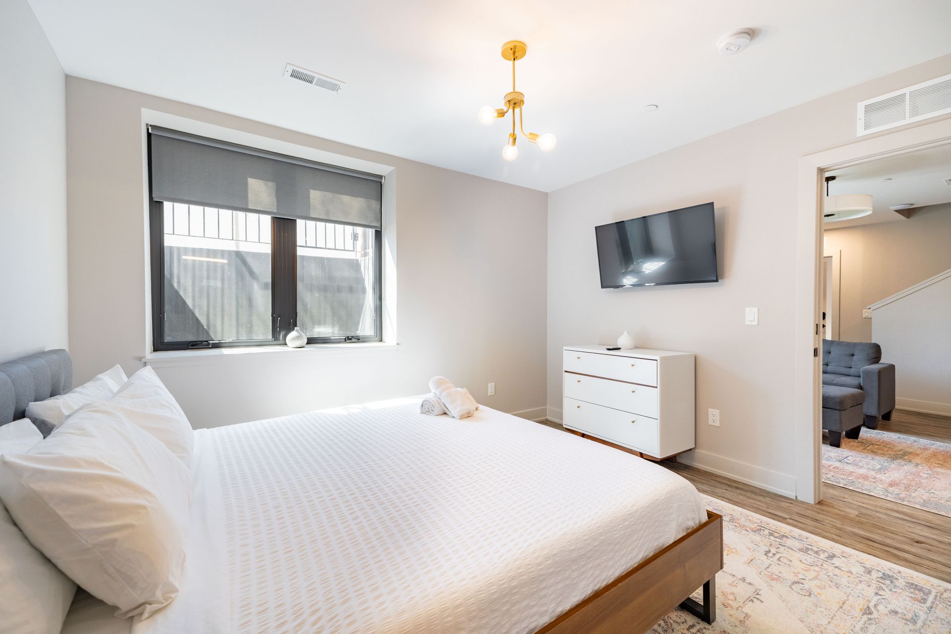 Bright bedroom with a bed, wall-mounted TV, dresser, window, and mirrored closet door