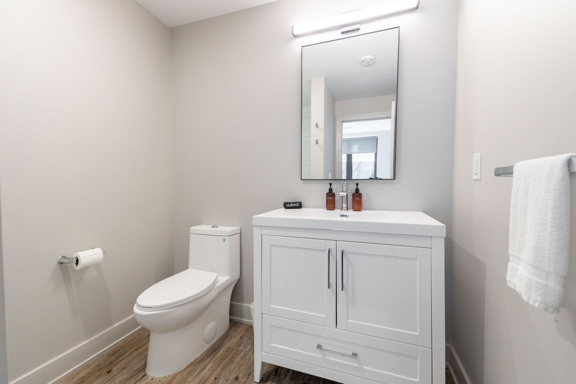 Bright modern bathroom with toilet, white vanity, mirror, and towel rack on gray walls.