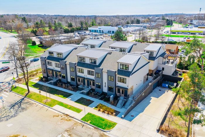 Aerial view of a large gray townhouse complex with sidewalks, lawns, and surrounding streets in a suburban area