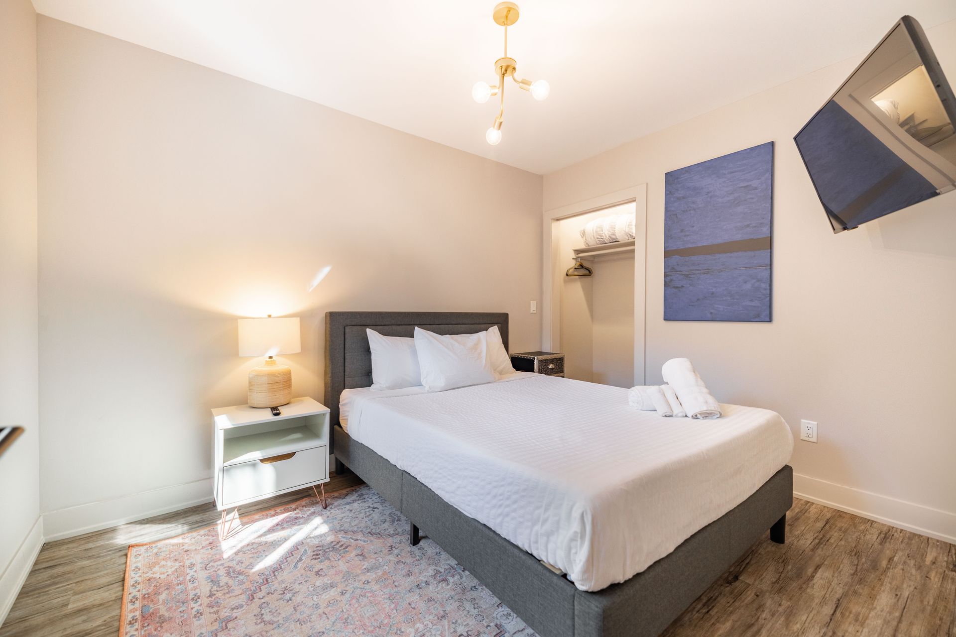 Bright bedroom with a neatly made bed, bedside lamp, wall art, and wall-mounted TV.