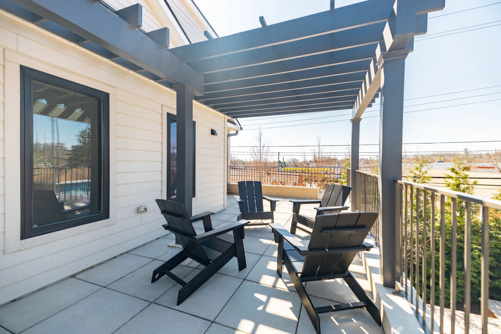 Small rooftop patio with black chairs, table, and striped awning beside a white house and metal railing.