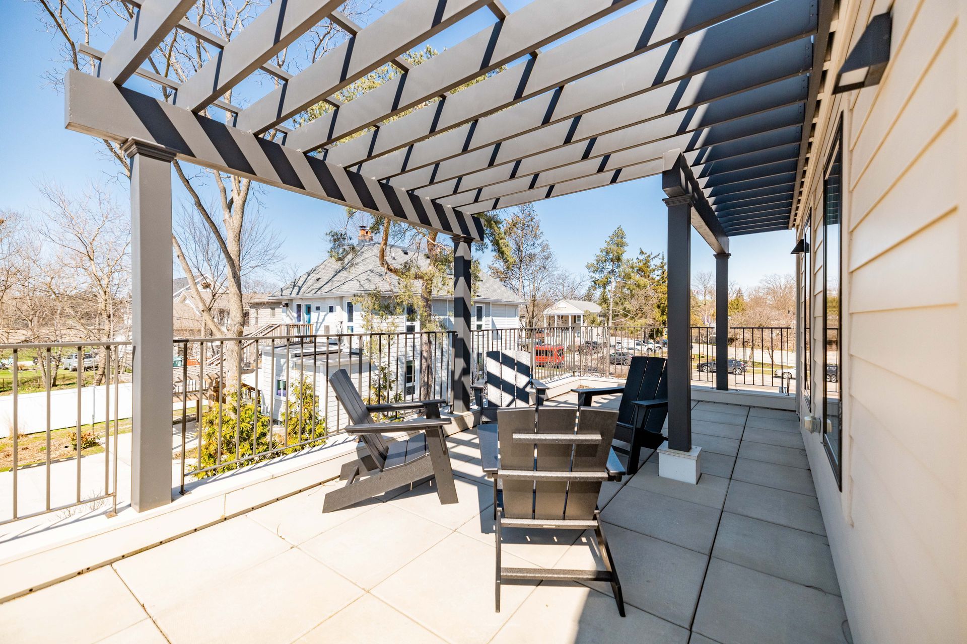 Covered patio with black chairs, pergola shade, and a view of the yard and street beyond