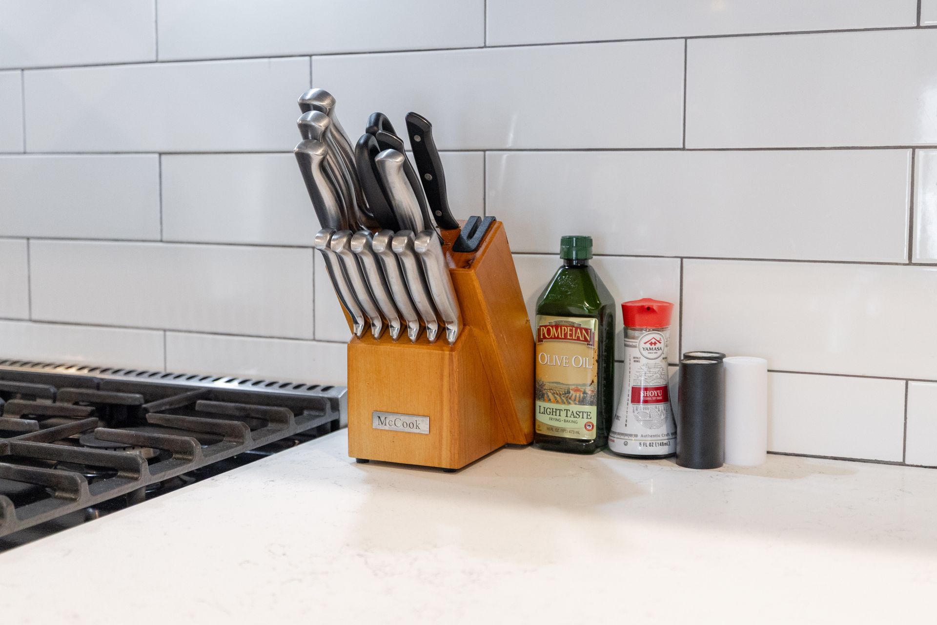 Kitchen countertop with knife block, bottle, spice jar, and pepper grinder beside a stovetop.