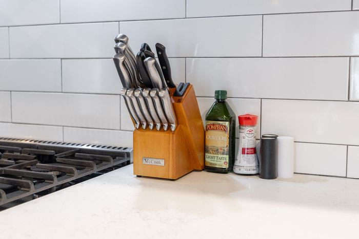 Kitchen countertop with knife block, bottle, spice jar, and pepper grinder beside a stovetop.