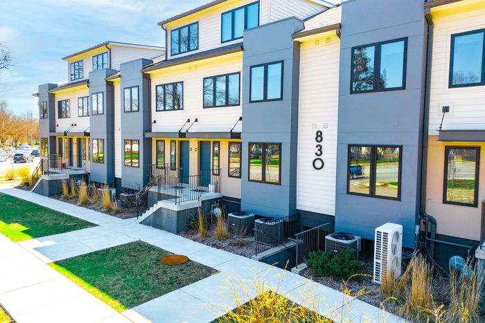 Modern apartment row with gray and yellow facades, balconies, and small front patios along a sidewalk