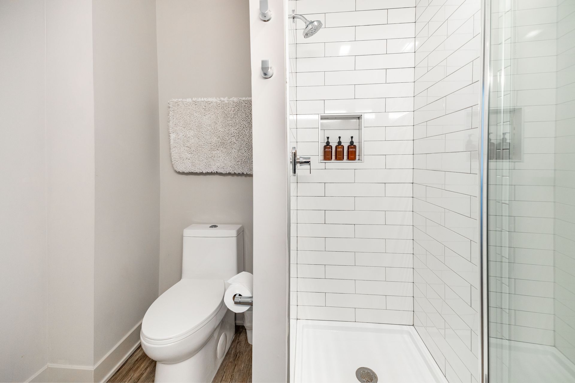 Small modern bathroom with toilet, walk-in shower, white tile, and wood floor.
