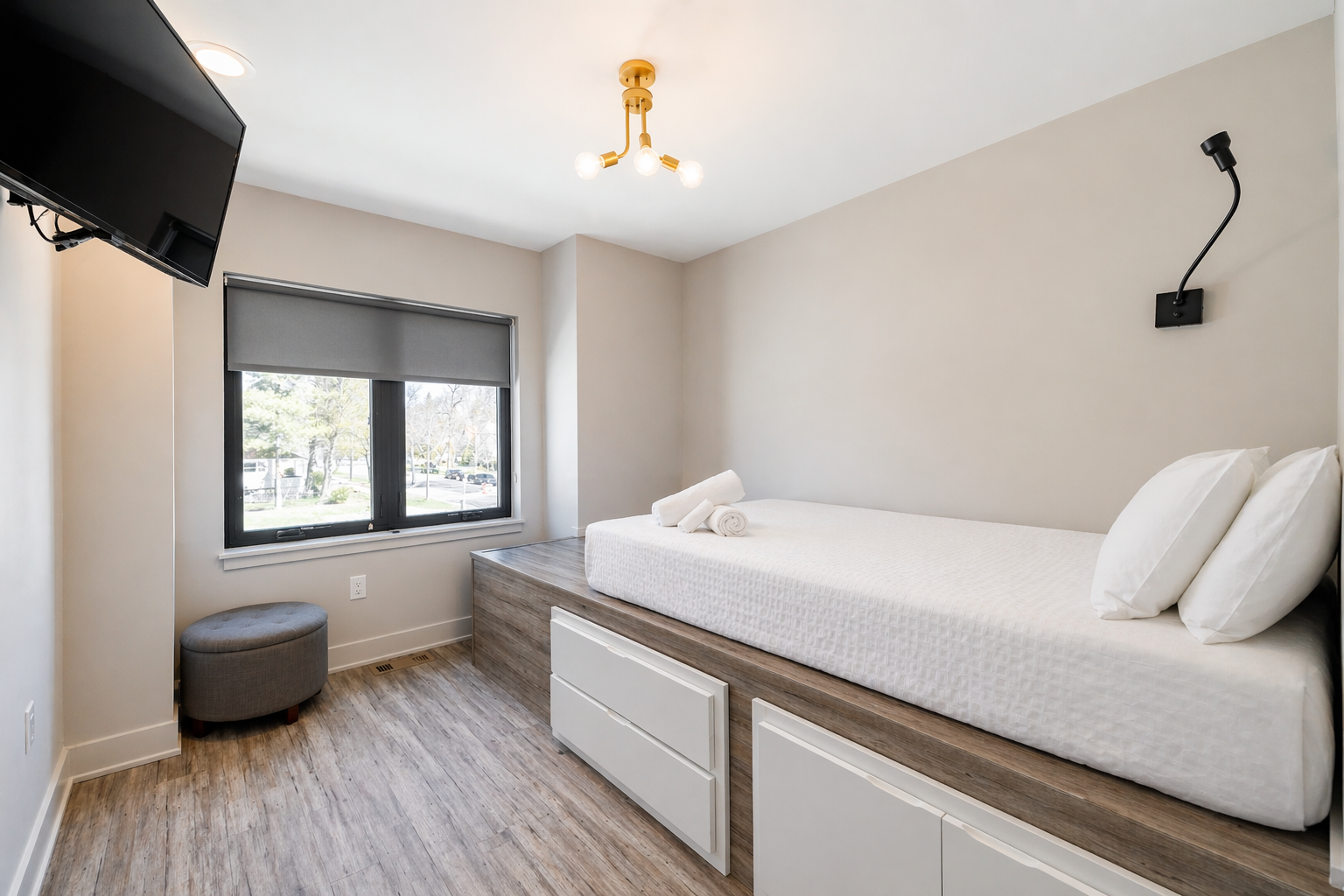 Bright modern bedroom with twin bed, window, wall-mounted TV, and light gray walls
