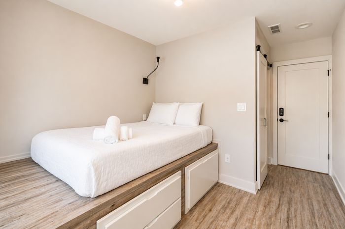 Bright minimalist bedroom with a white bed, wood floor, and doorway to the hall