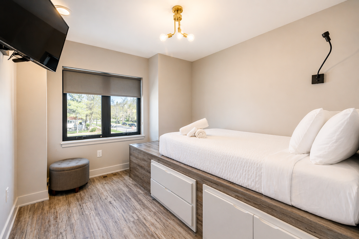 Small bedroom with a twin bed, window, wall-mounted TV, and neutral decor