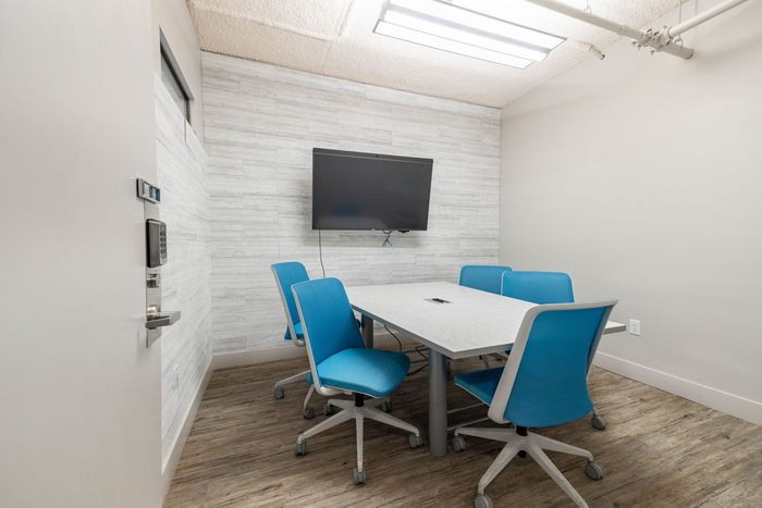 Modern conference room with blue chairs, white table, wall-mounted TV, and white brick walls.