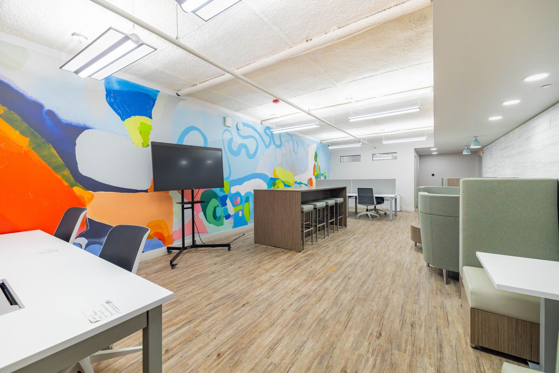 Colorful modern office lounge with mural wall, wood floors, desks, and green booth seating
