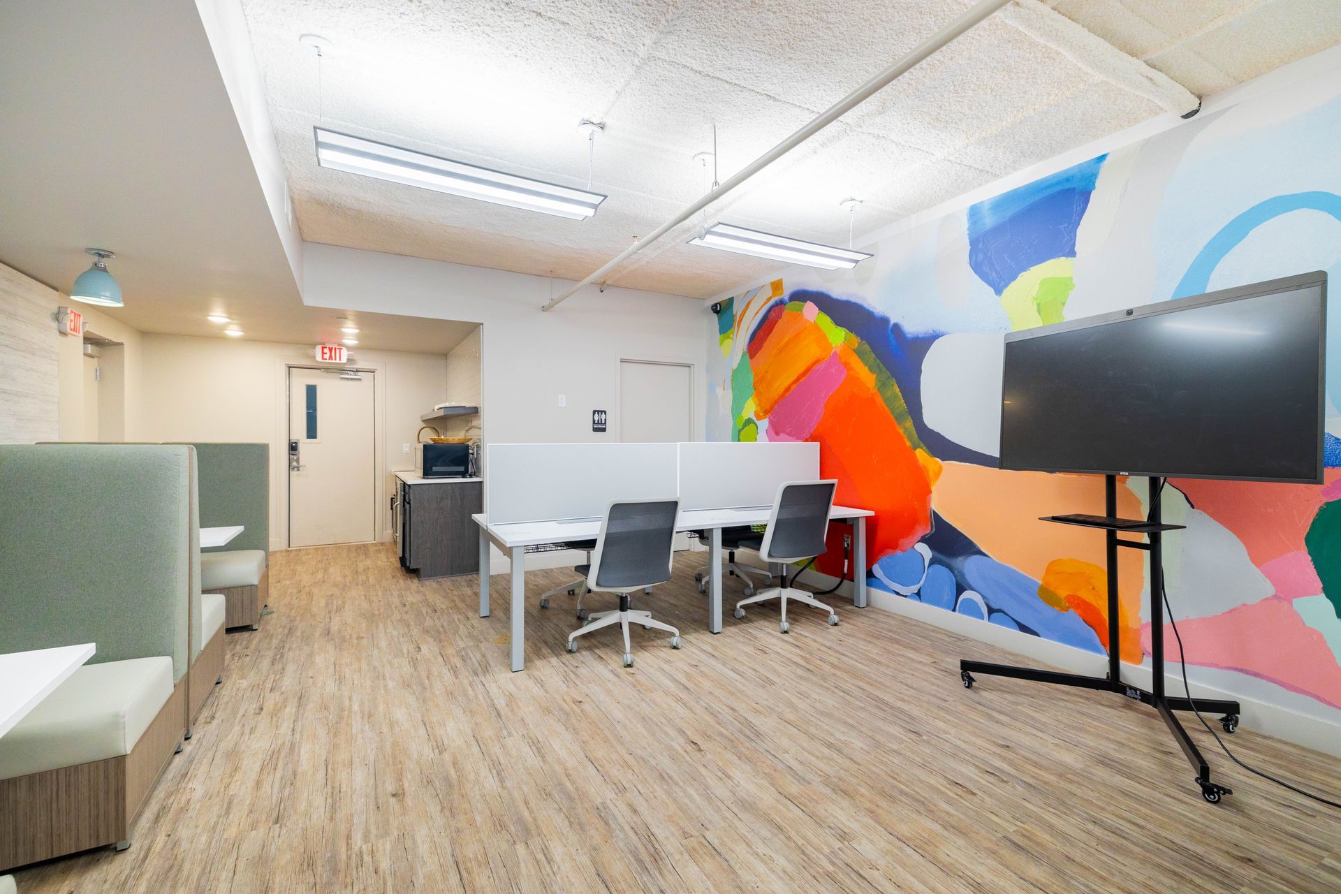 Bright office lounge with colorful mural, white table and chairs, and a TV on a stand
