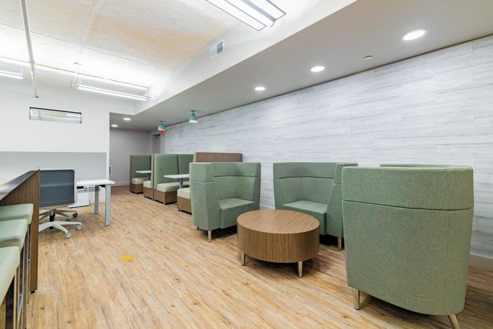 Modern lounge with green booths, round wooden tables, and wood flooring under bright ceiling lights