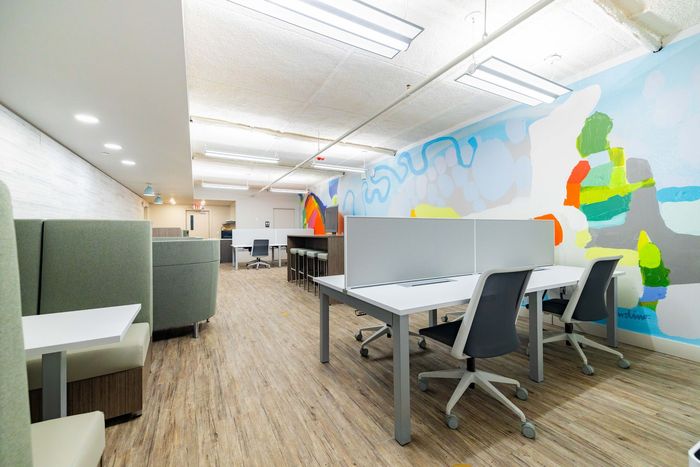 Modern office interior with desks, chairs, wood floors, and colorful wall art to the right