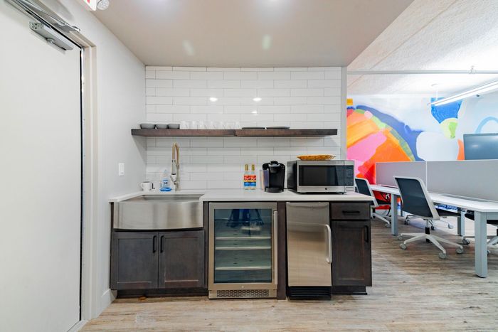 Breakroom with sink, mini fridge, microwave, countertop, and colorful mural wall next to tables and chairs