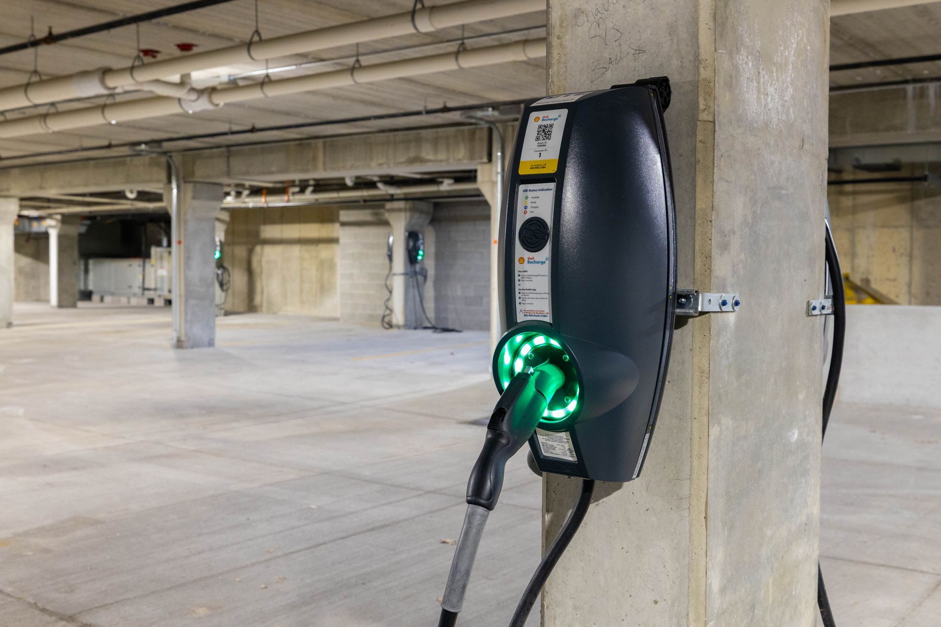 Electric vehicle charging station mounted on a concrete pillar in an empty parking garage.