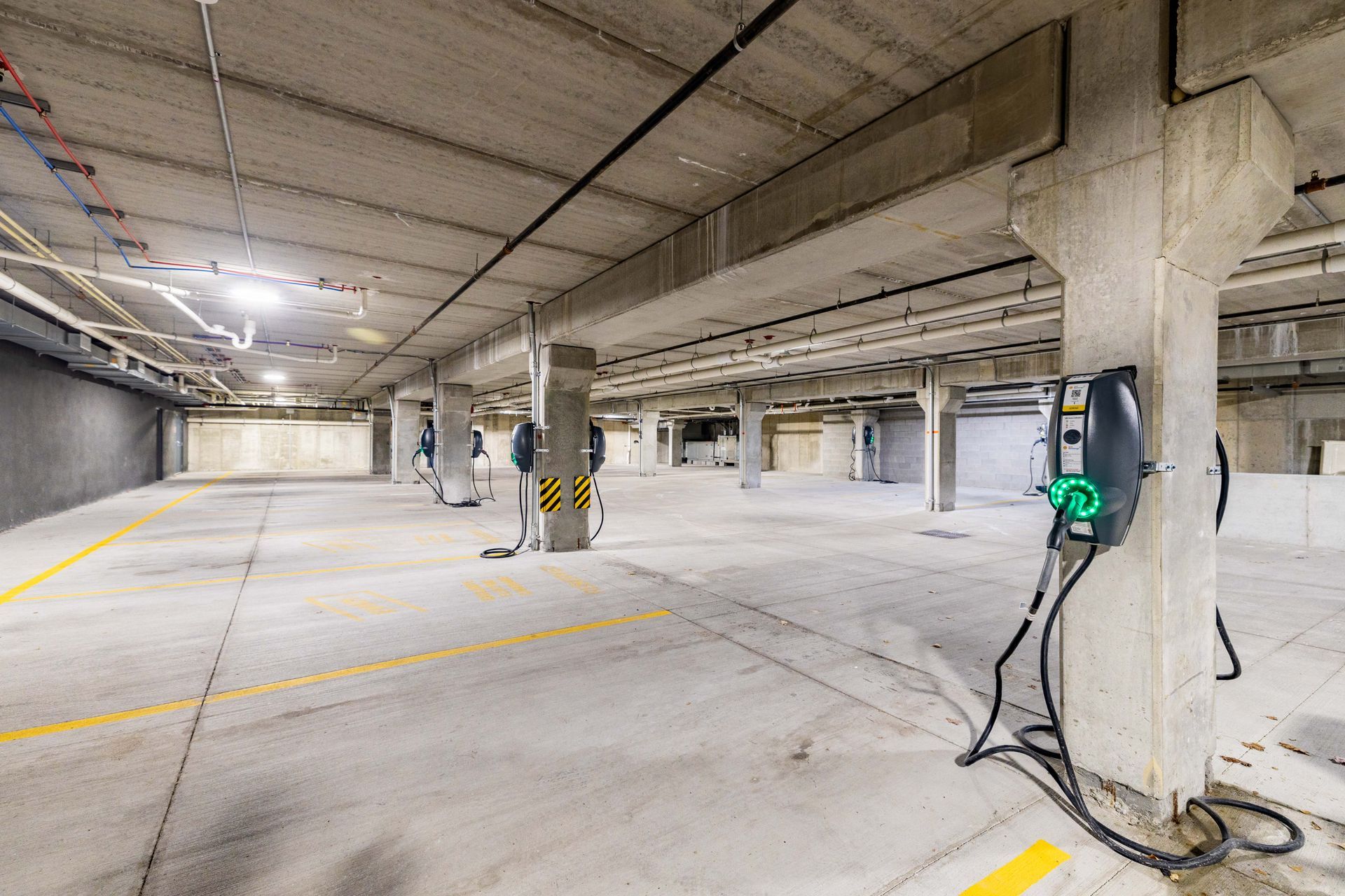 Empty underground parking garage with concrete pillars and a green EV charging station.