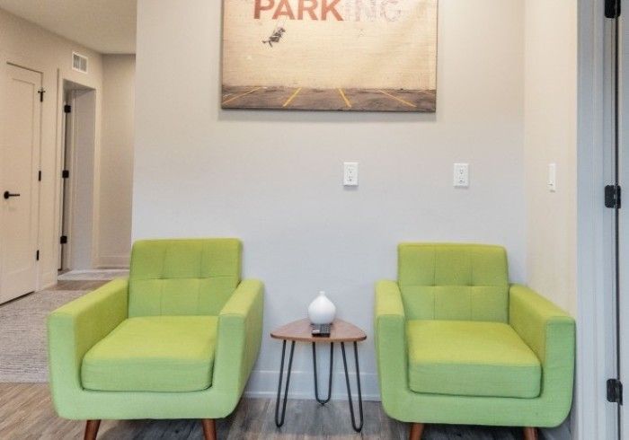 Two lime green armchairs flank a small table with a decorative vase, beneath a 