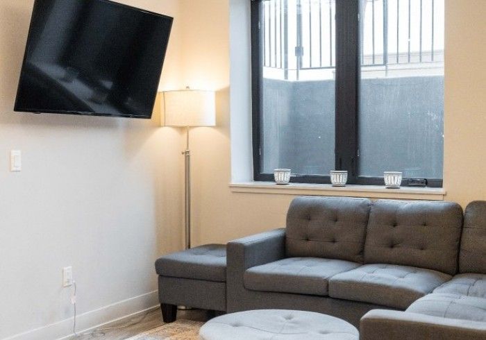 Gray sectional sofa in a living room with a mounted TV, a lamp, and a window.
