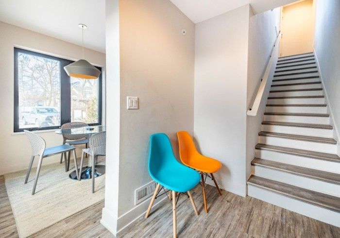 Entryway with stairs, teal and orange chairs, table, and a large window.