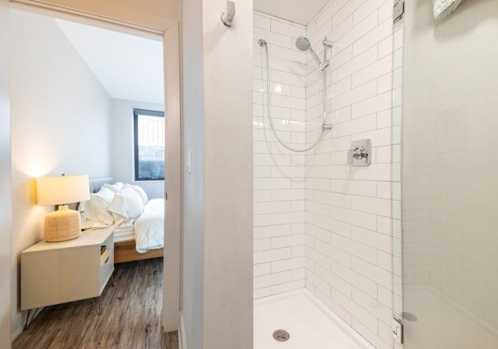 Bathroom with white subway tile shower and bedroom in background.