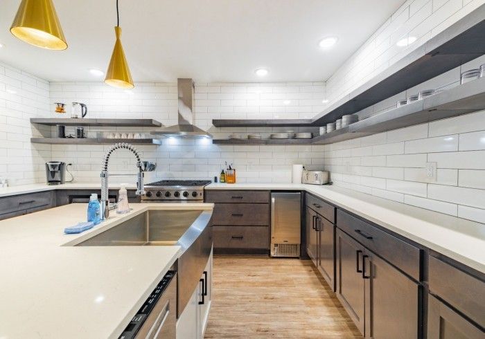 Modern kitchen with white tile backsplash, dark cabinets, island sink, and pendant lights