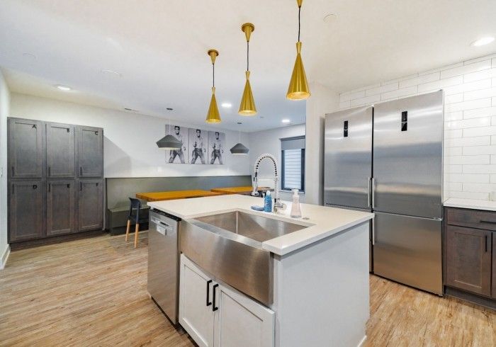 A modern kitchen featuring a central island with a farmhouse sink, stainless appliances, and lockers along the wall.