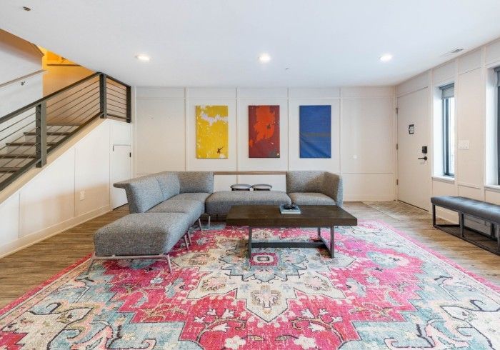 A modern lounge with a gray sectional, dark wood coffee table, and a large, colorful pink and teal rug under wall art.
