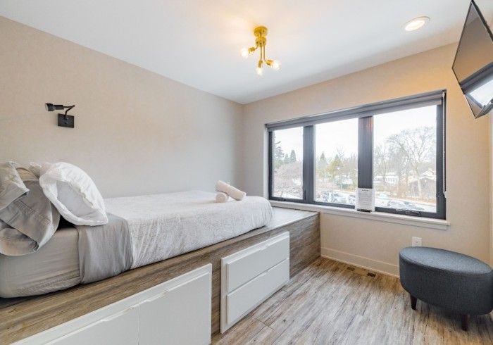 Bedroom with a low bed, drawers, window, TV, and a round stool.